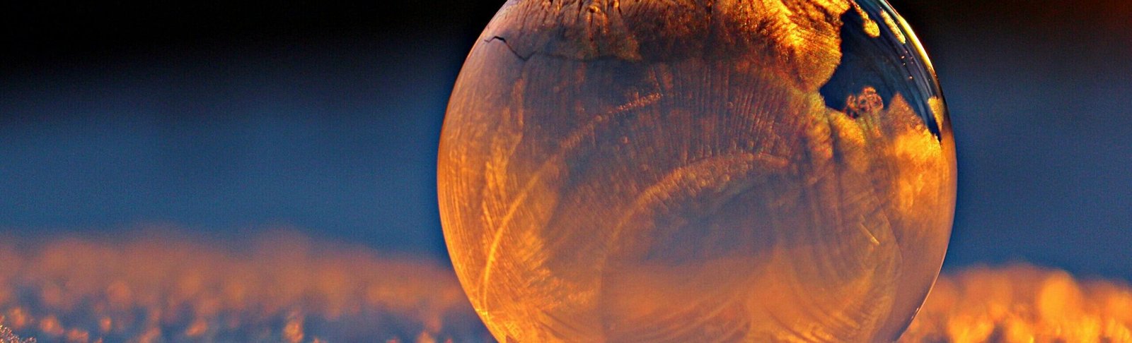 Close-up shot of a frozen bubble with warm reflections resting on a snowy surface at twilight.